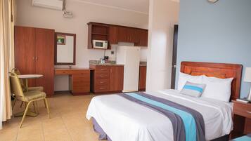 A hotel room with a bed, a desk, a chair, a microwave, and a refrigerator.