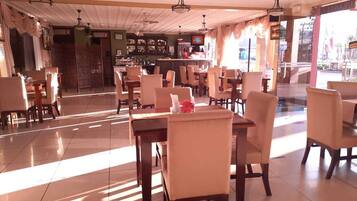 A spacious restaurant with multiple dining tables and chairs, a bar area, and a view of the street outside.