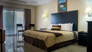 A hotel room with a large bed, a desk, a chair, and a window with curtains.
