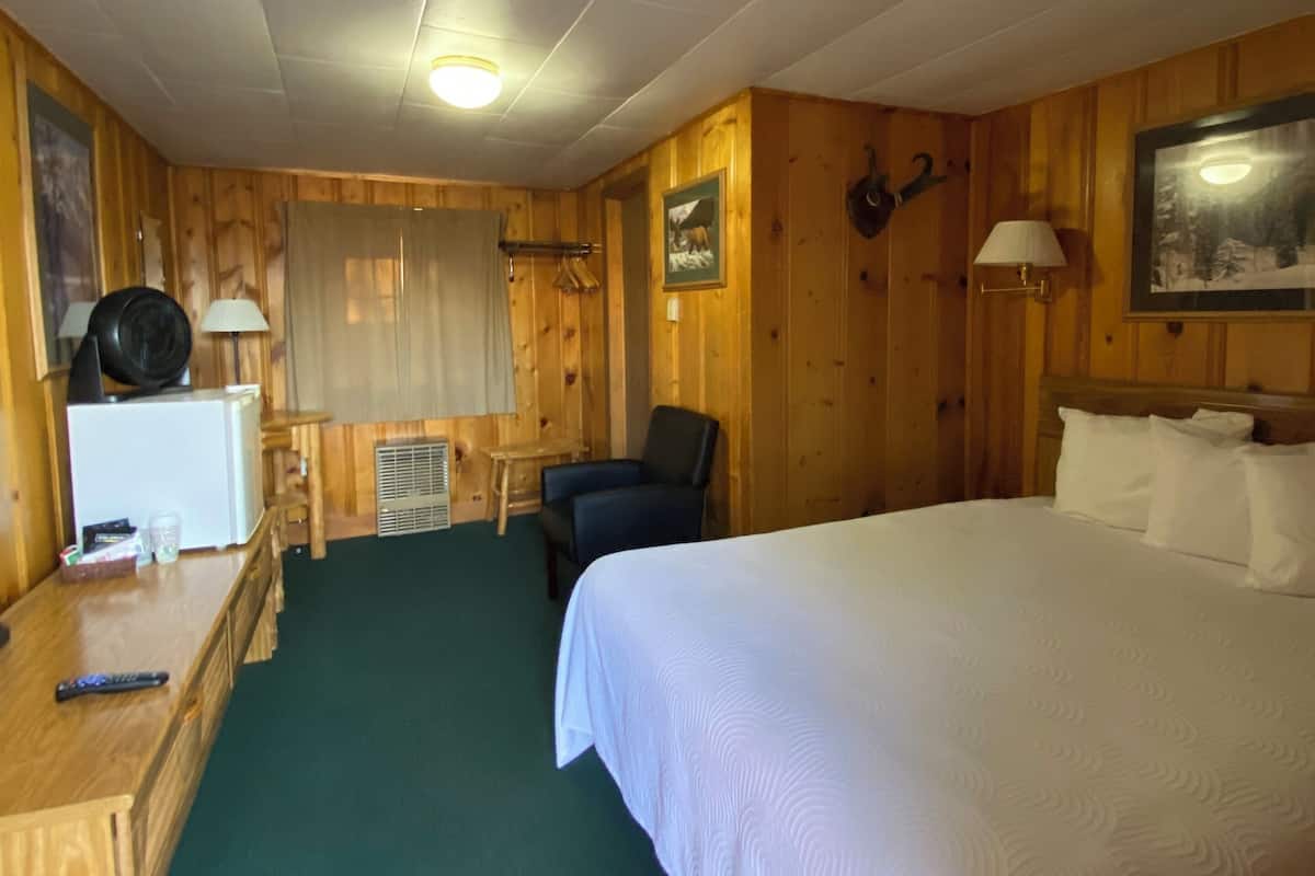 A wooden-paneled room with a bed, a desk, a chair, and a lamp.