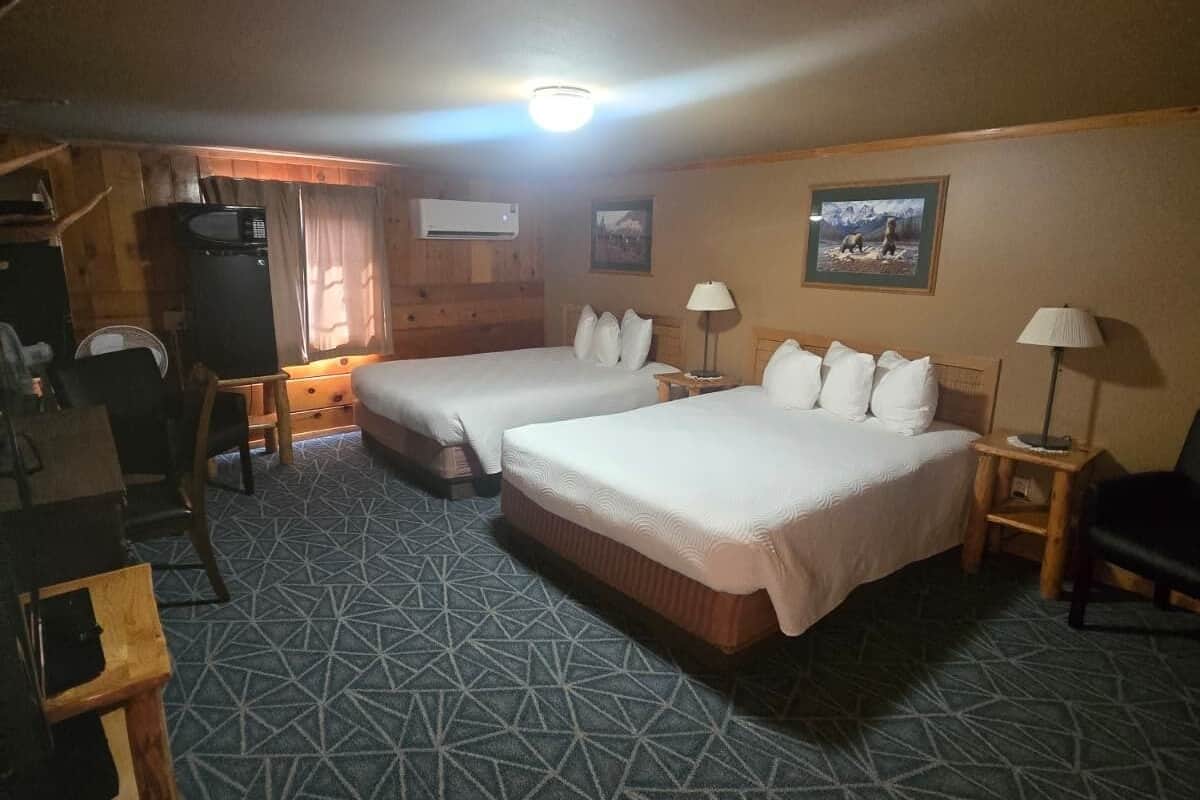 A hotel room with two beds, a desk, a chair, a lamp, and a picture on the wall.