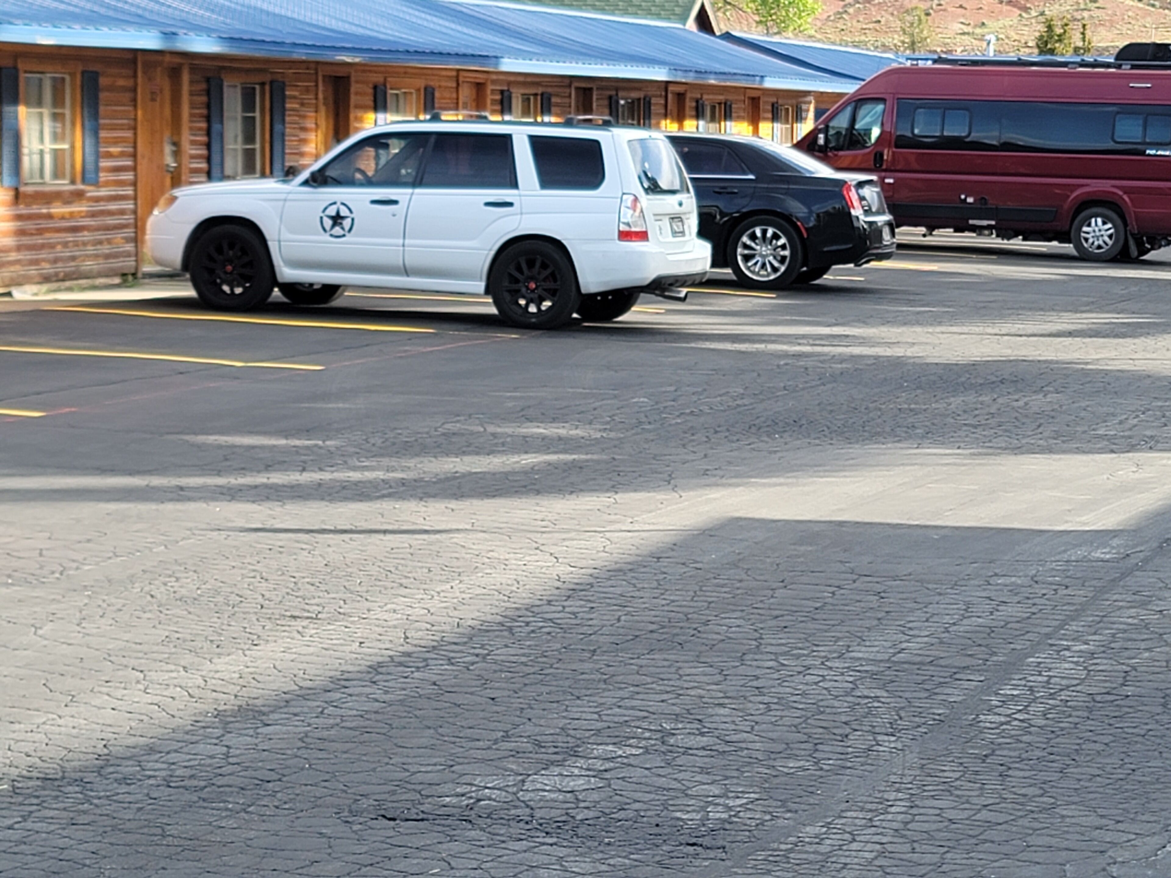 A parking lot with a white SUV and a maroon RV.