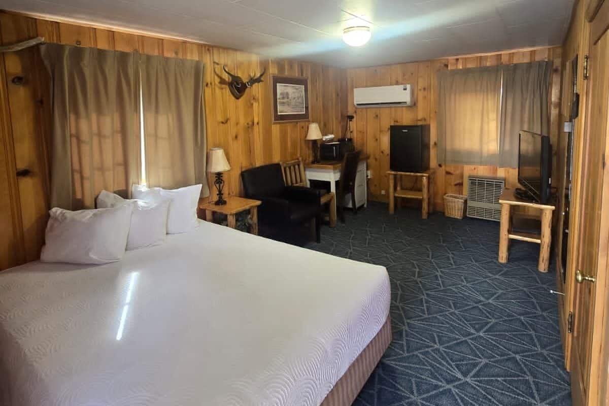 A hotel room with a large bed, a desk with a chair, a television, and a small table.