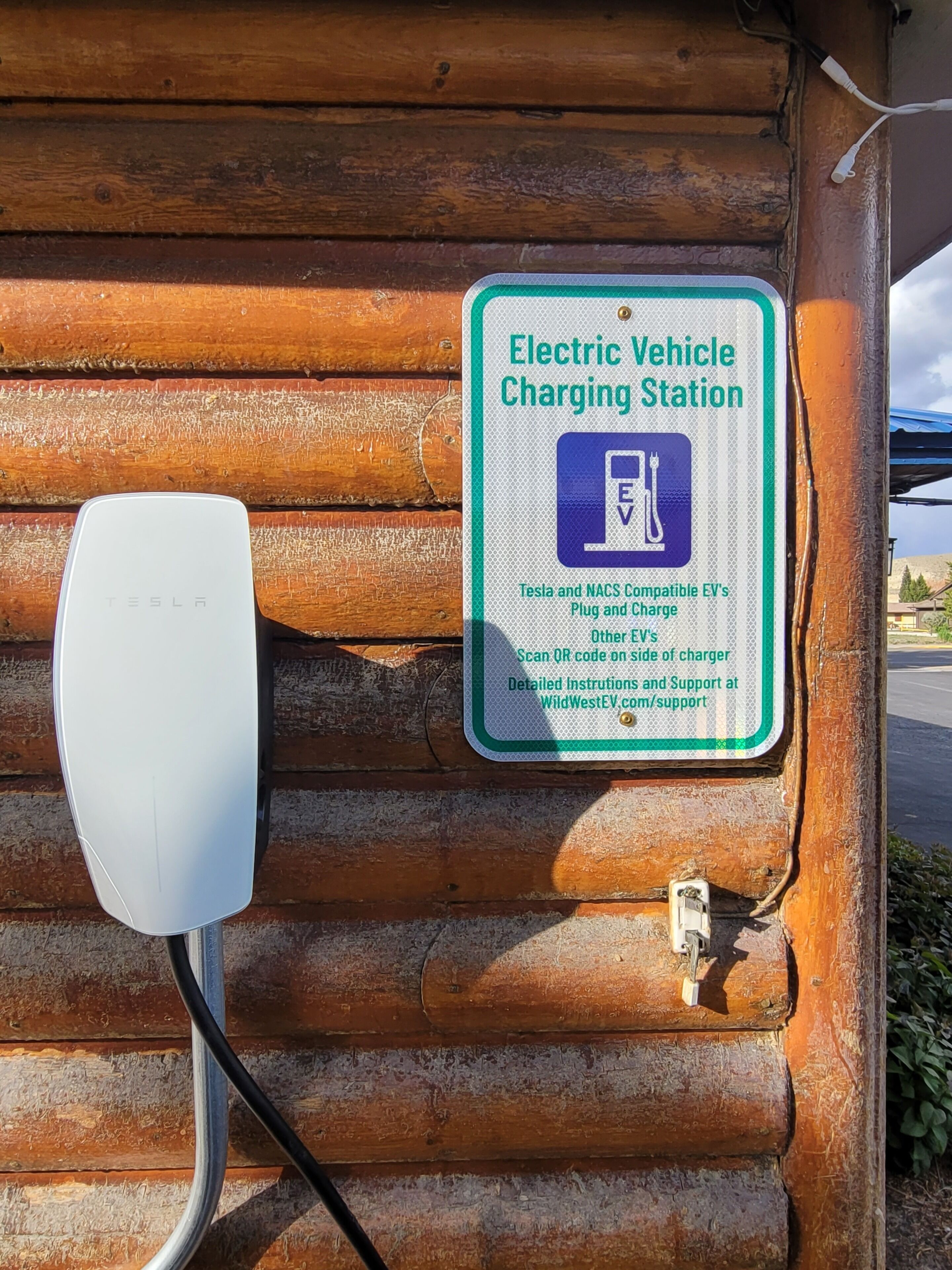 Una estación de carga para vehículos eléctricos con un cartel que indica compatibilidad con vehículos Tesla y NACS.