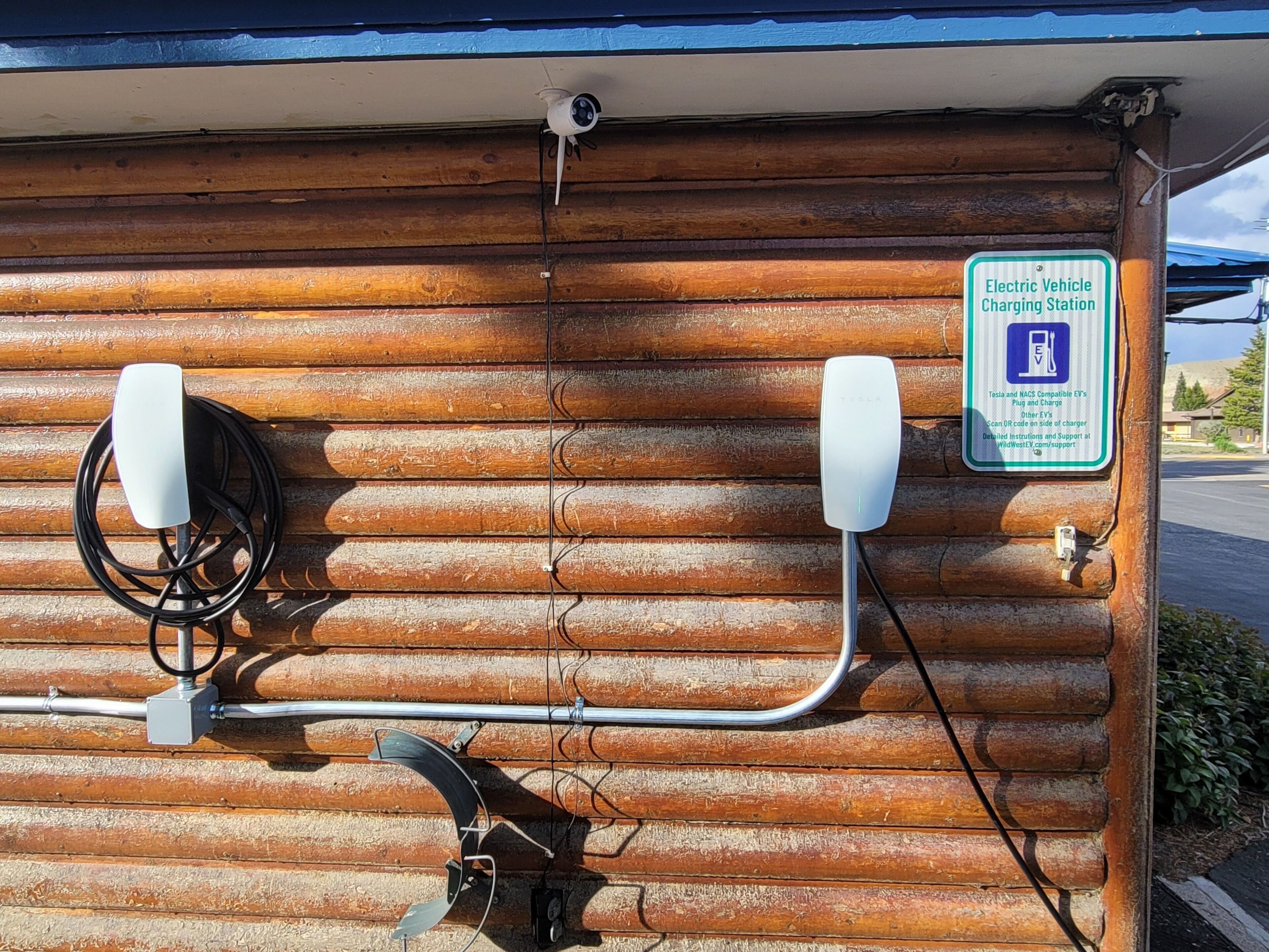 An electric vehicle charging station with a sign indicating compatibility with Tesla and NACS EVs.