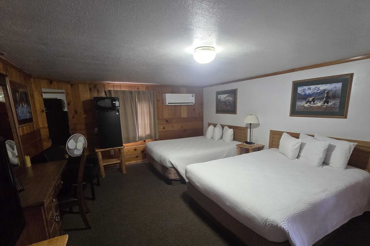 A hotel room with two beds, a desk, a chair, a fan, an air conditioning unit, and a ceiling light.