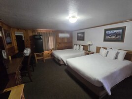 Habitación de hotel con dos camas, un escritorio, una silla, un ventilador, un equipo de aire acondicionado y una lámpara de techo.