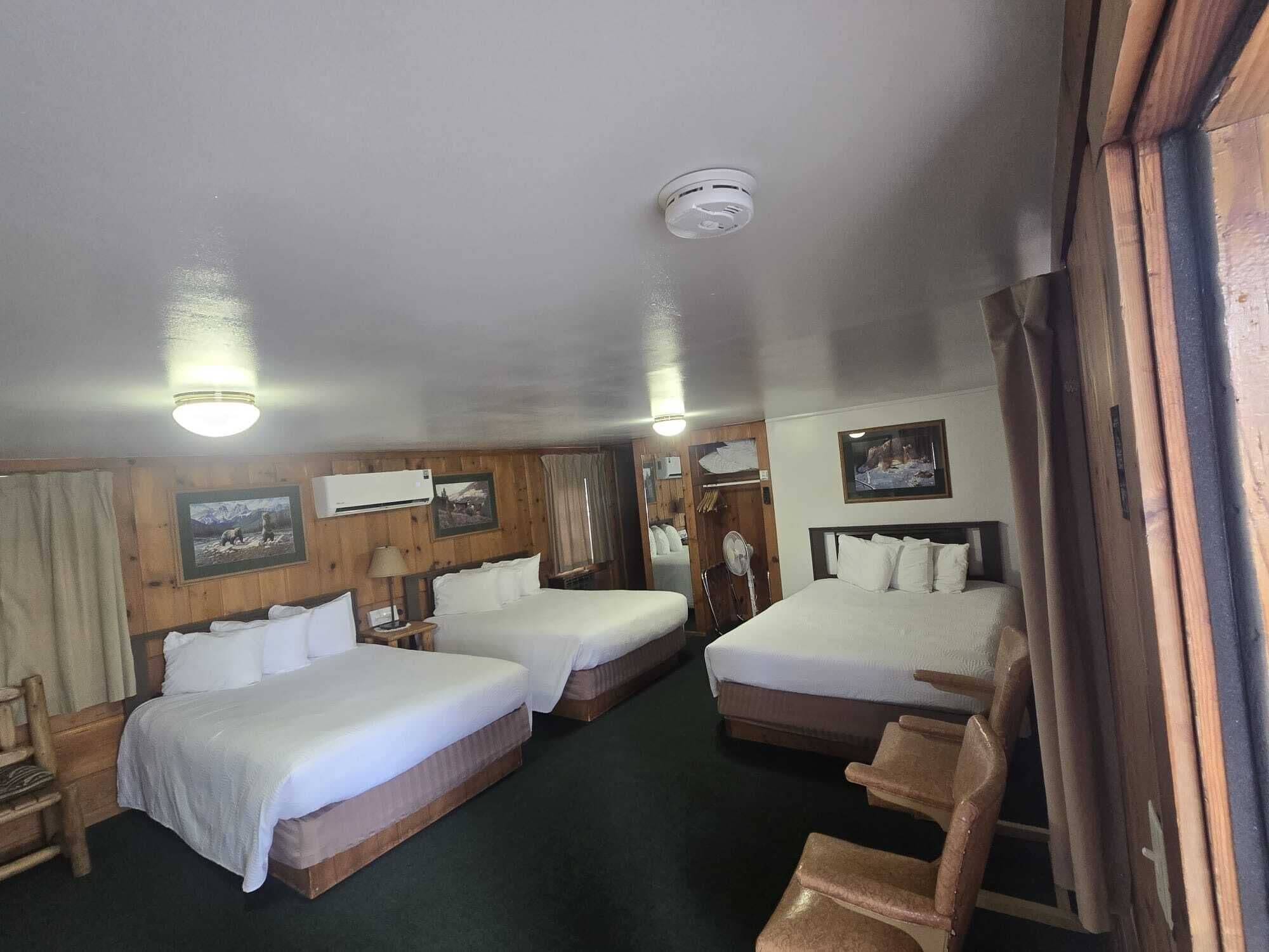 A hotel room with two beds, wooden walls, a ceiling fan, and a mounted air conditioner.