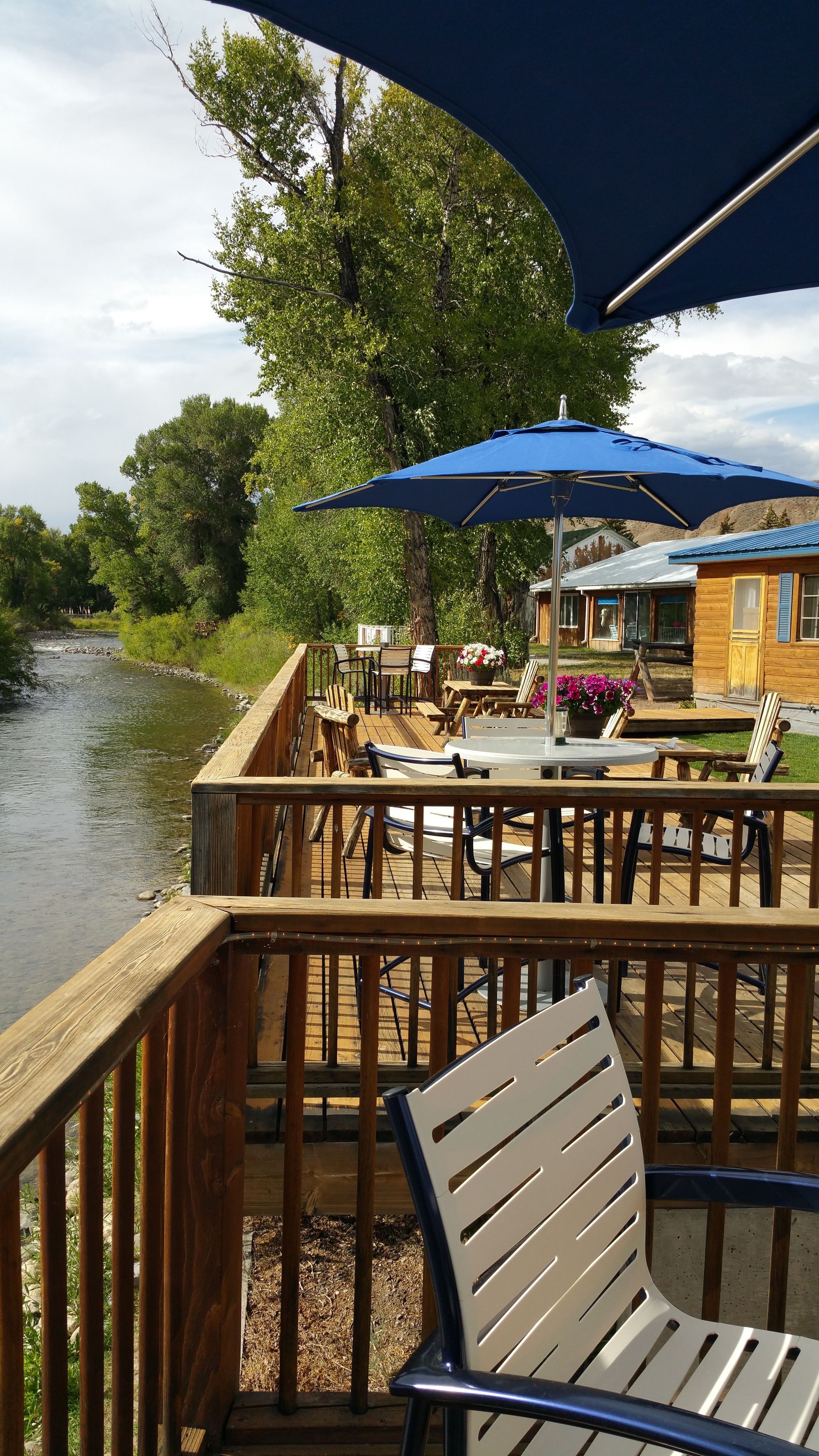 A wooden deck with outdoor seating, overlooking a river, and a building with a blue roof.