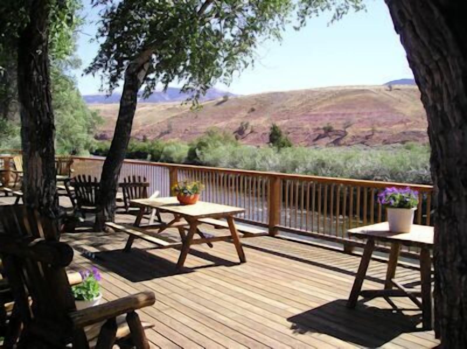 A wooden deck with outdoor seating, overlooking a river and hilly landscape.