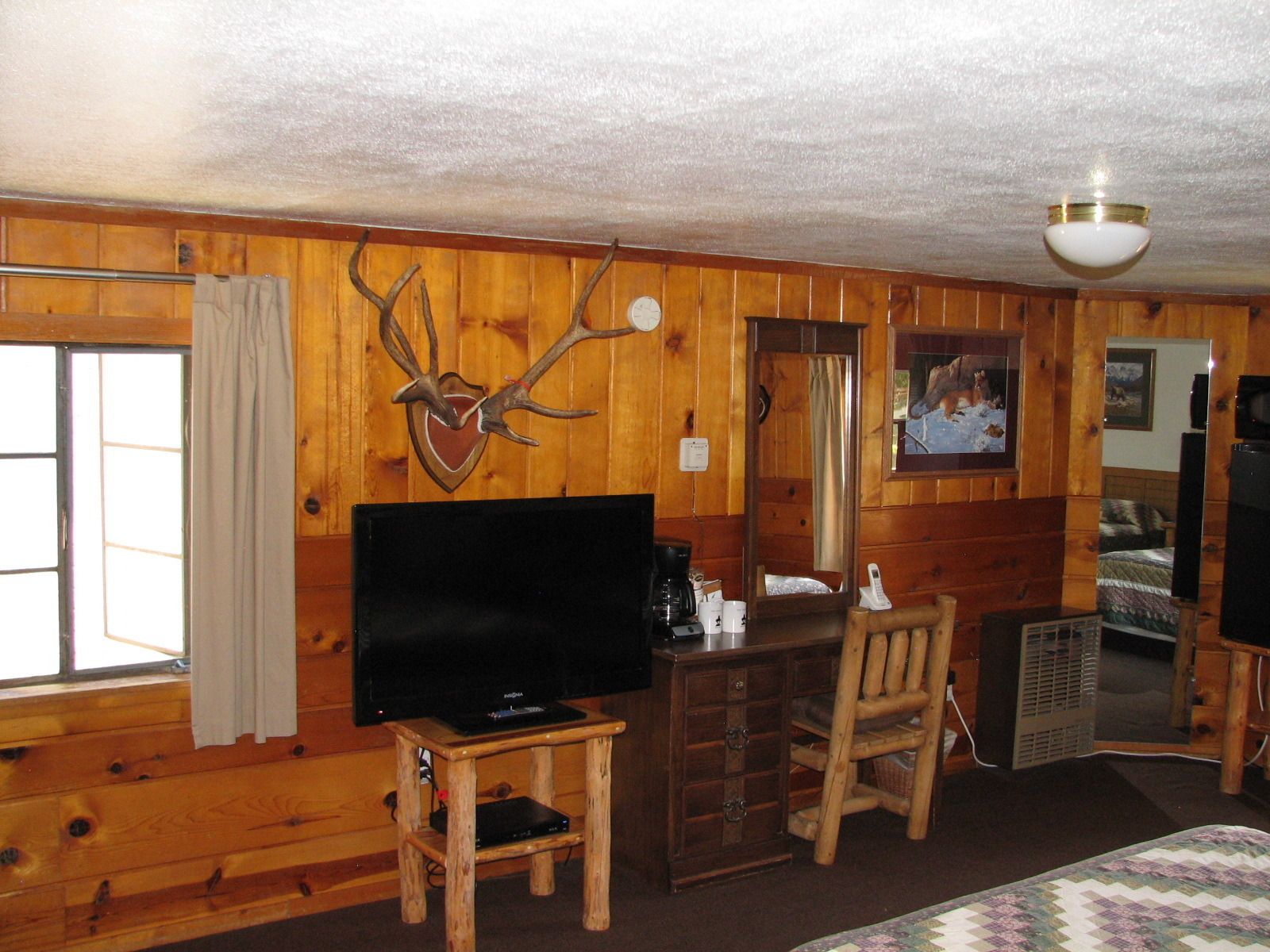 Ein Holzblockhaus-Innenraum mit einem Fernseher auf einem Holztischchen, einem Holzstuhl, einem kleinen Tisch, einem Spiegel und einem Kamin.