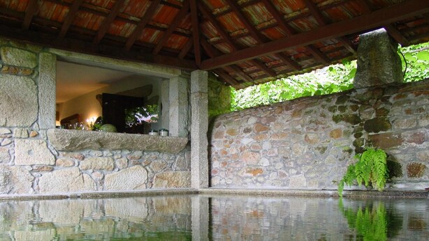 A stone-walled pool with a clear reflection, a stone bench, and a thatched roof structure.