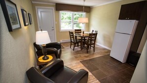 A compact kitchen with a dining area, a refrigerator, and a seating arrangement including a chair and a table. - Studiotel Bromont (Bromont)