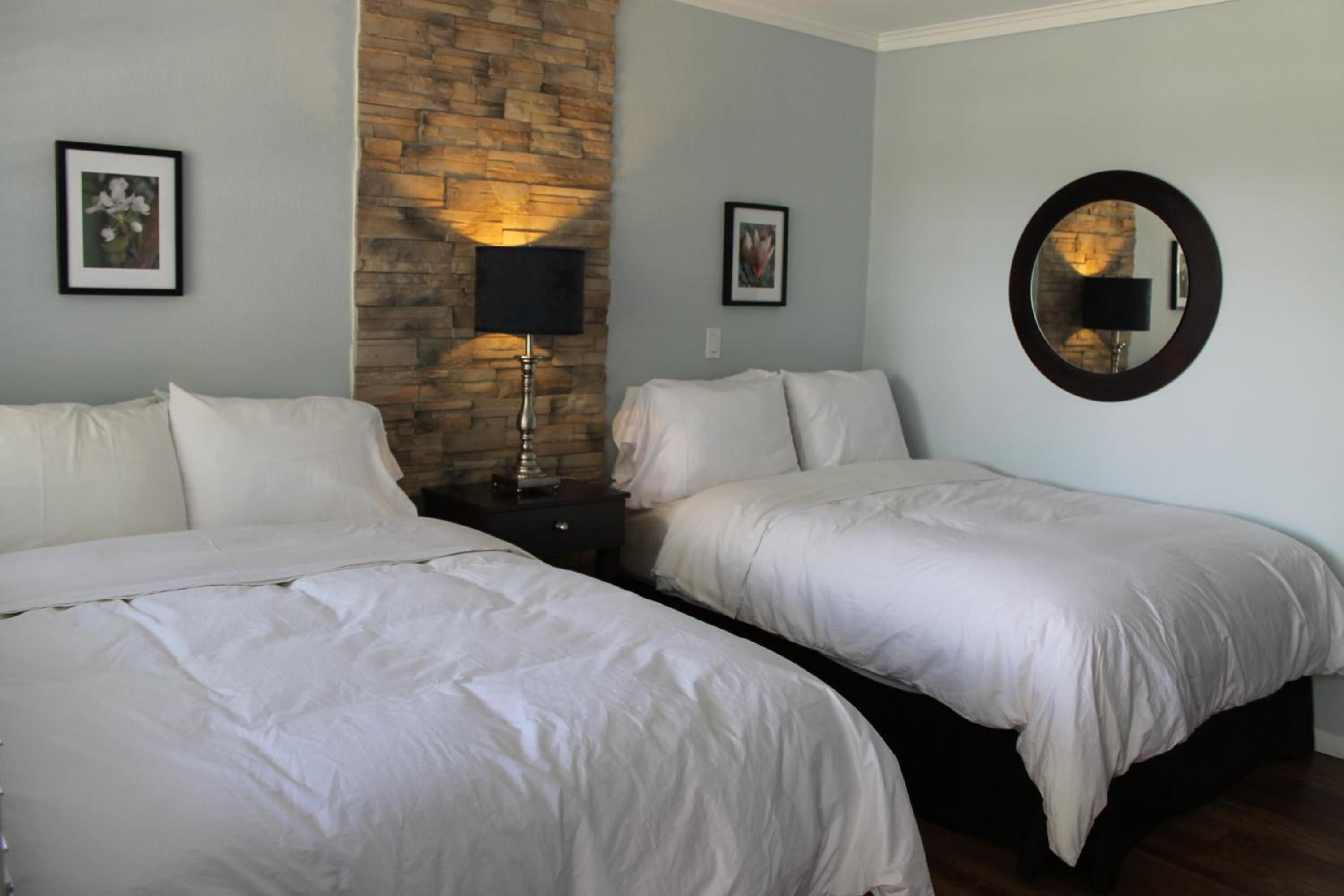 Habitación de hotel con dos camas, una pared de acento de piedra, cuadros enmarcados y un espejo redondo.