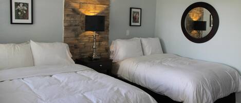 Habitación de hotel con dos camas, una pared de acento de piedra, cuadros enmarcados y un espejo redondo.