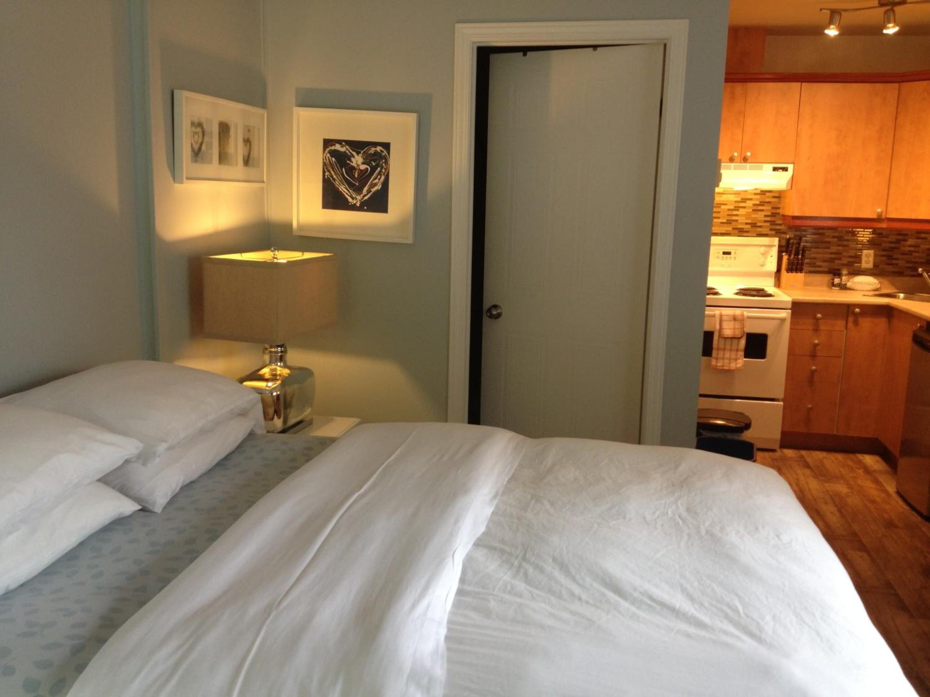 Une chambre à coucher avec un lit, une table de chevet avec une lampe et une porte donnant sur la cuisine.
