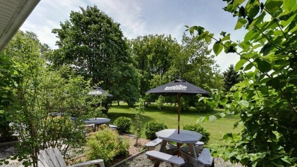 A patio area with outdoor seating, including a table and chairs, and a large umbrella. - Studiotel Bromont (Bromont)