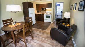A compact kitchen with a refrigerator, microwave, and stove. There is a dining table with chairs and a sofa with a lamp. - Studiotel Bromont (Bromont)