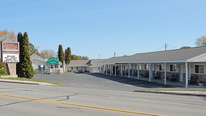 A motel with a green sign, a parking lot, and a row of rooms with covered porches.
