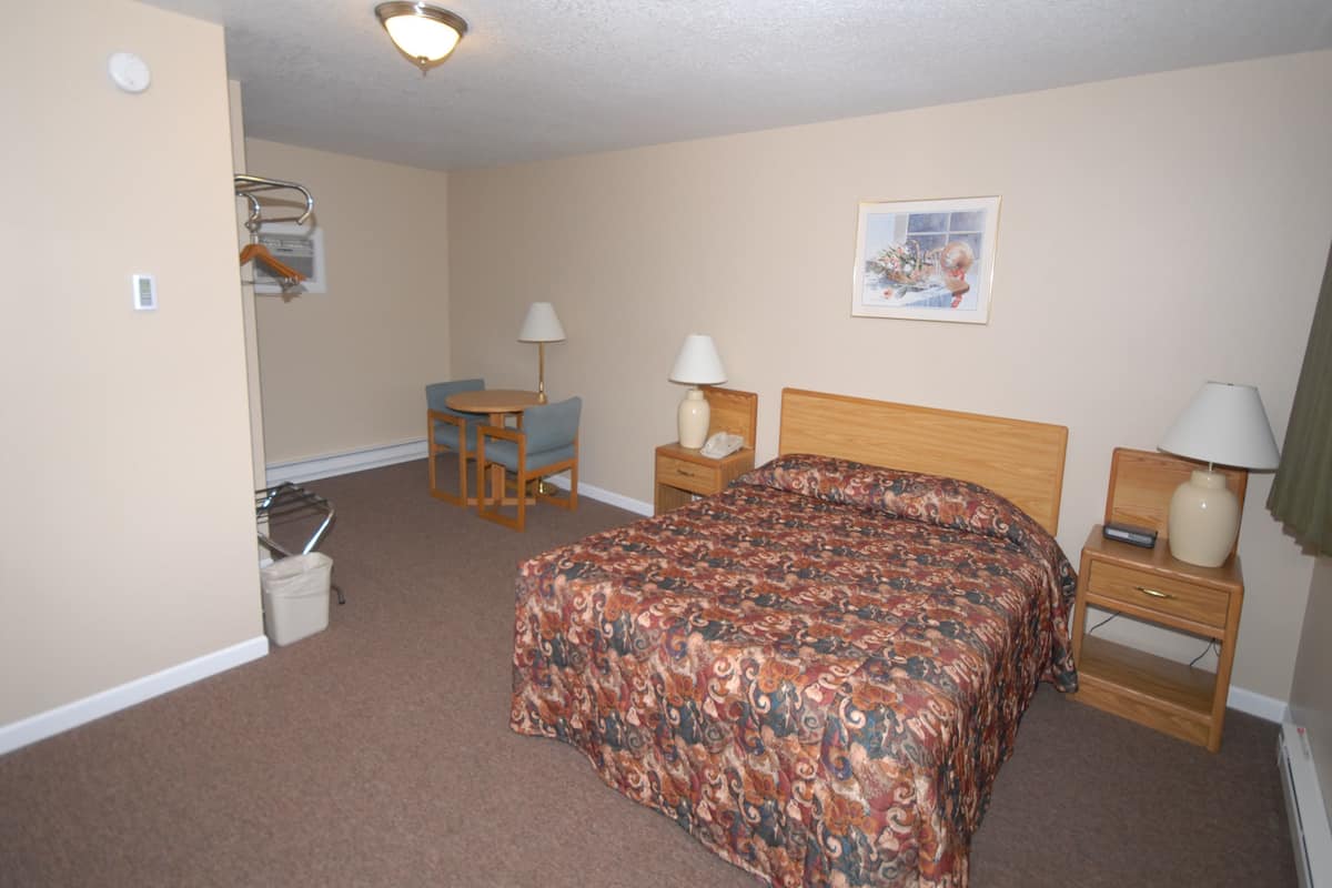 A hotel room with a bed, two bedside tables, a chair, a small table, a lamp, a picture on the wall, and a ceiling light.