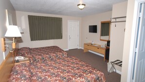 A hotel room with a bed, a desk, a chair, a TV, and a bathroom.