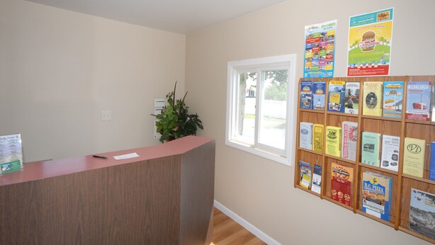 A reception area with a wooden desk, a bulletin board with various notices, a potted plant, and a window.