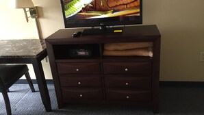 Un televisor sobre un mueble de madera, con un control remoto, una lámpara y una silla.
