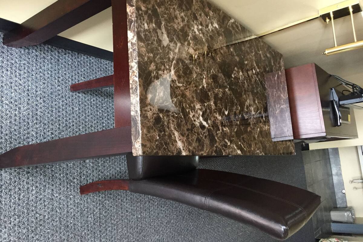 A dining table with a marble top, dark wooden chairs, and a small cabinet with a red top.