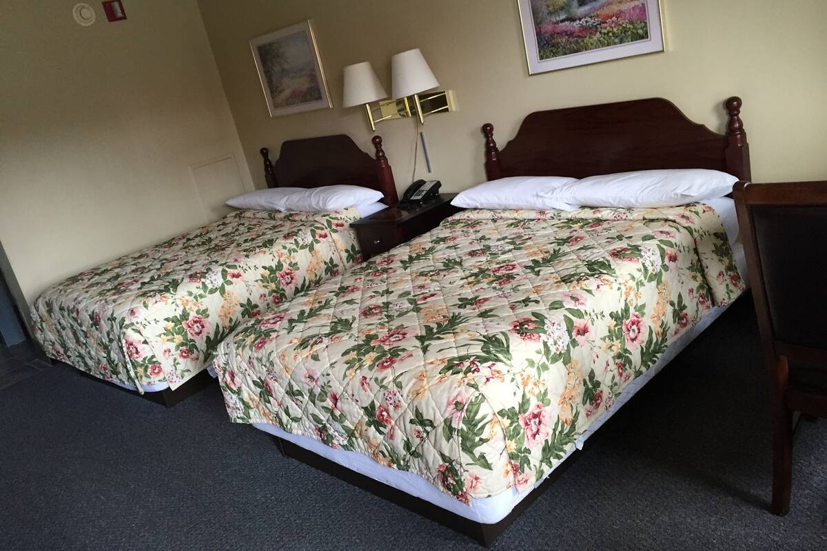 A double bed with floral bedding, a bedside table, a lamp, and a painting on the wall.