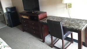 Una habitación de hotel con escritorio, televisión, refrigerador pequeño y lámpara.