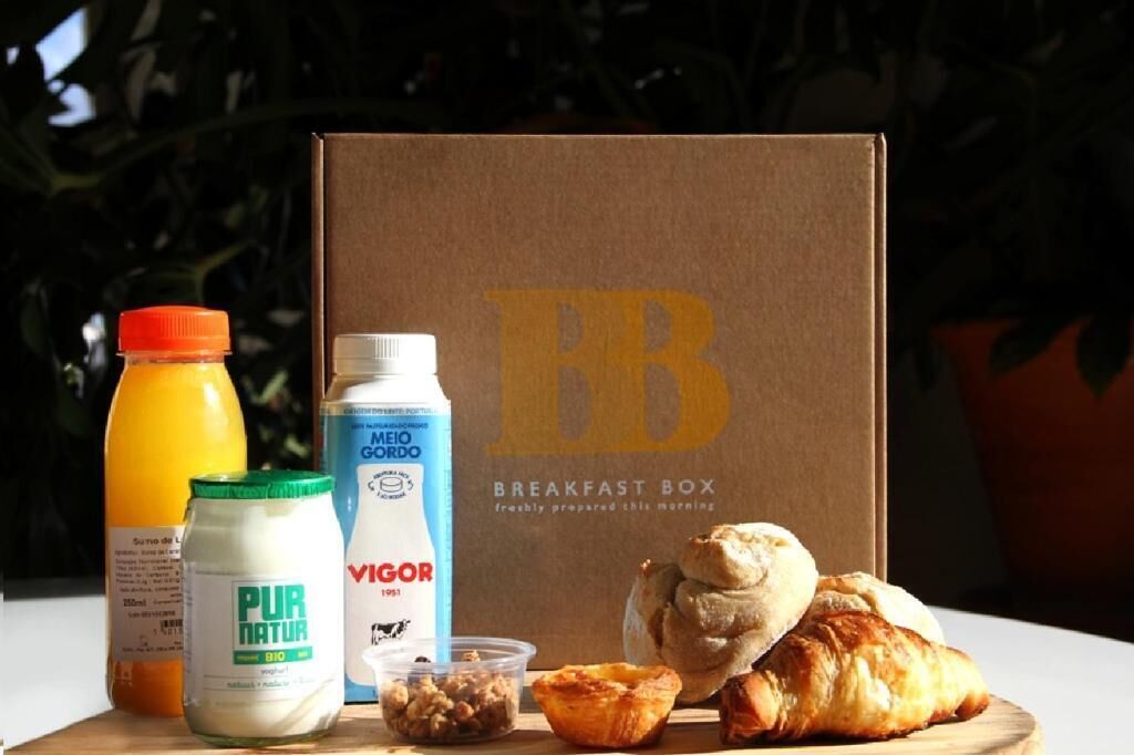 Une boîte de petit-déjeuner contenant un carton de lait, une bouteille de jus d’orange, un pot de yaourt, un récipient de noix et des croissants.