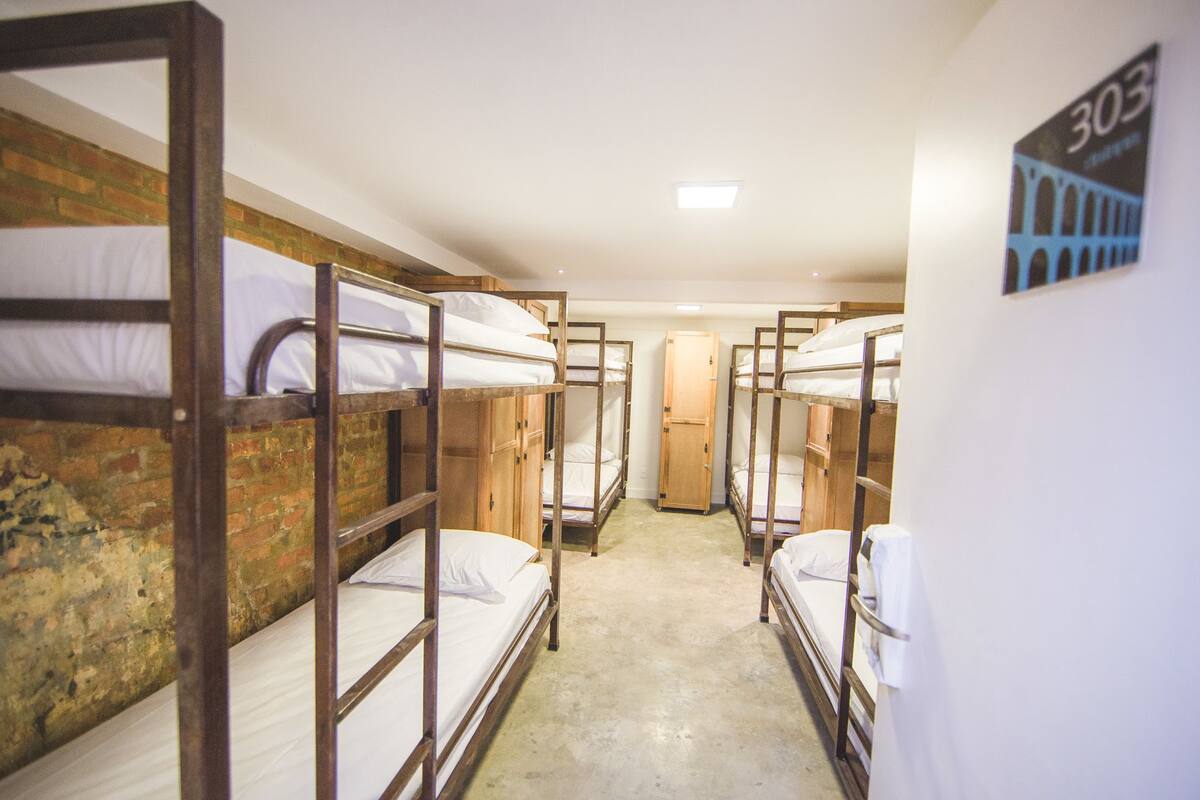 A dormitory room with bunk beds, a brick wall, and a door.