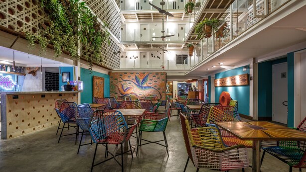 A spacious indoor area with multiple tables and colorful chairs, a ceiling fan, and hanging plants. - Da Lapa Design Hotel - Hostel (Rio de Janeiro)
