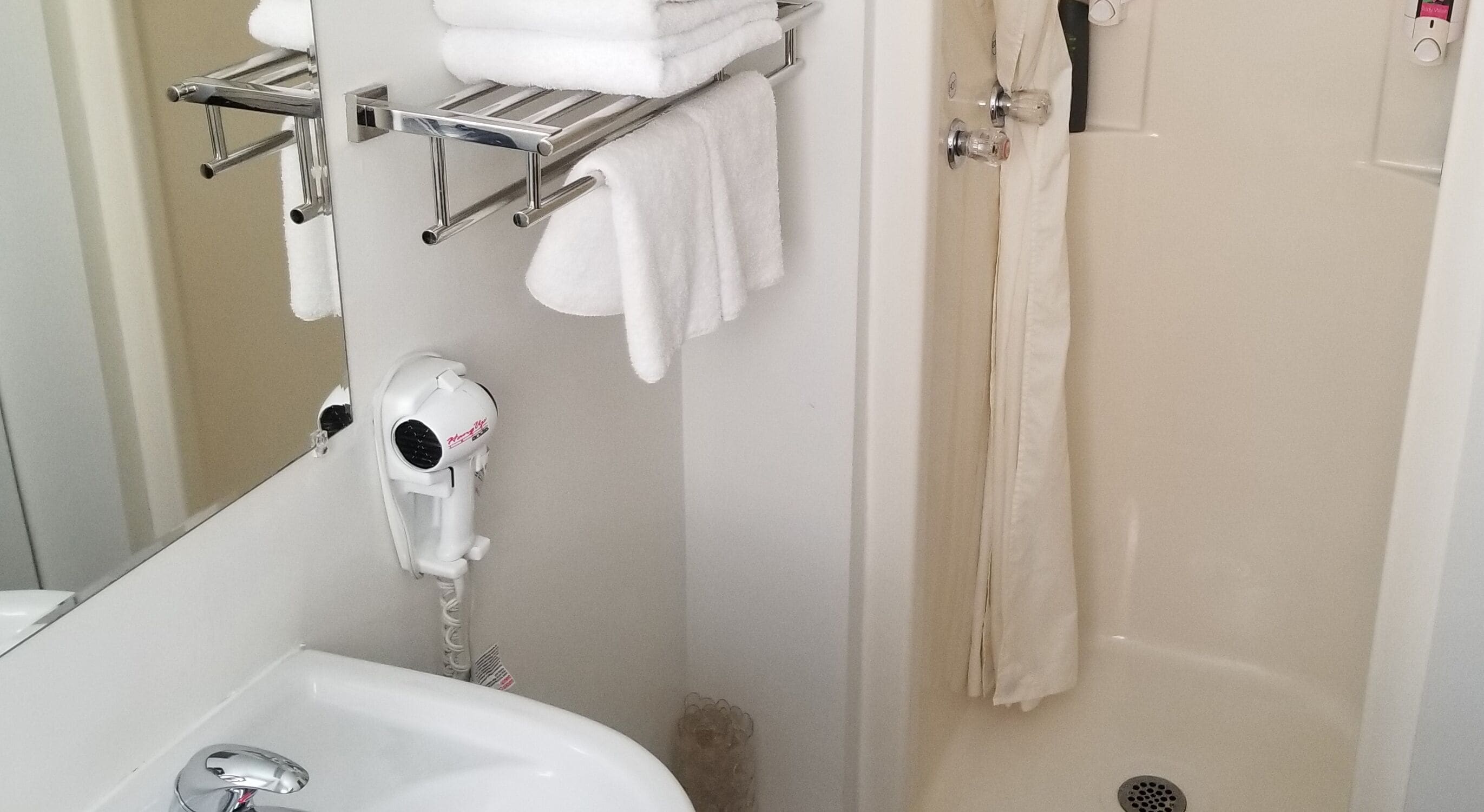 Un baño con lavamanos, secador de pelo, toallero y cortina de ducha.
