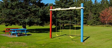 Un parque con mesas de picnic, columpios y un juego de columpios rojo y azul.
