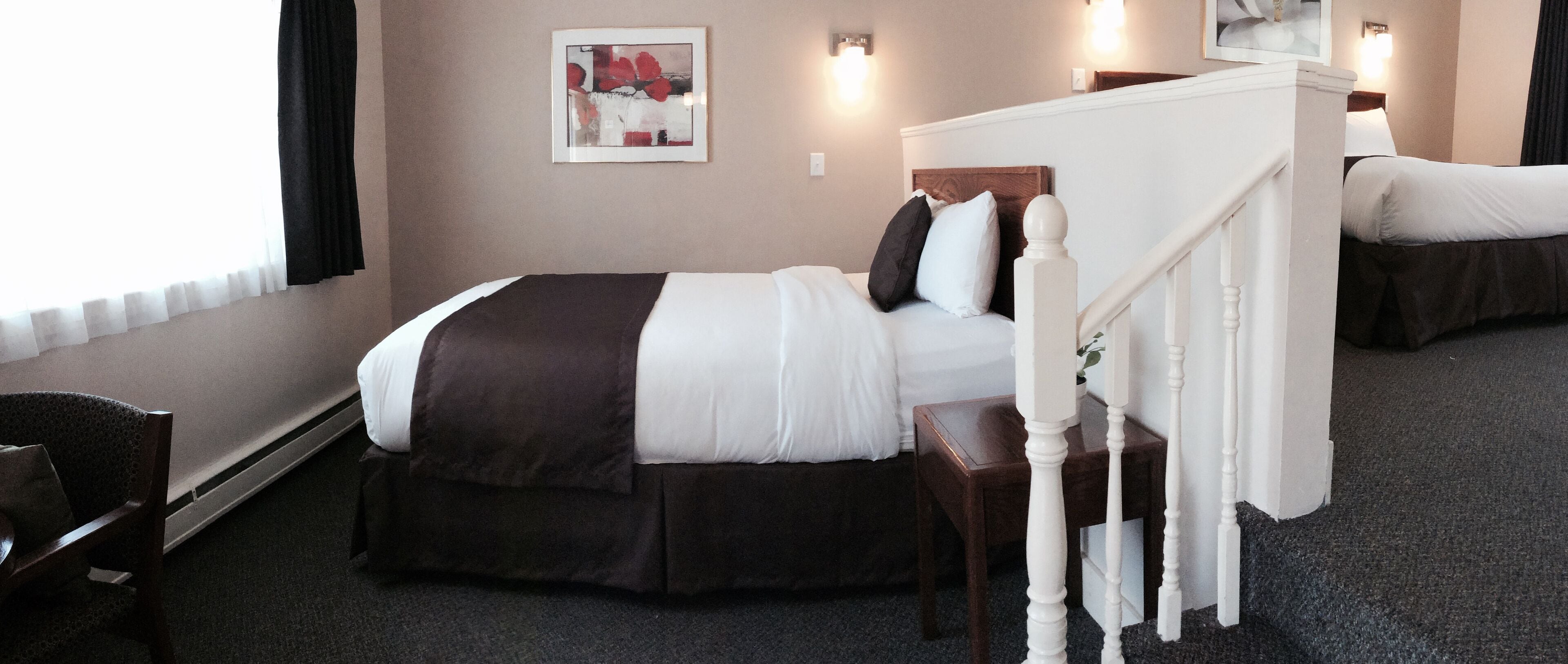 Una habitación de hotel con cama, una silla, una escalera y un cuadro en la pared.