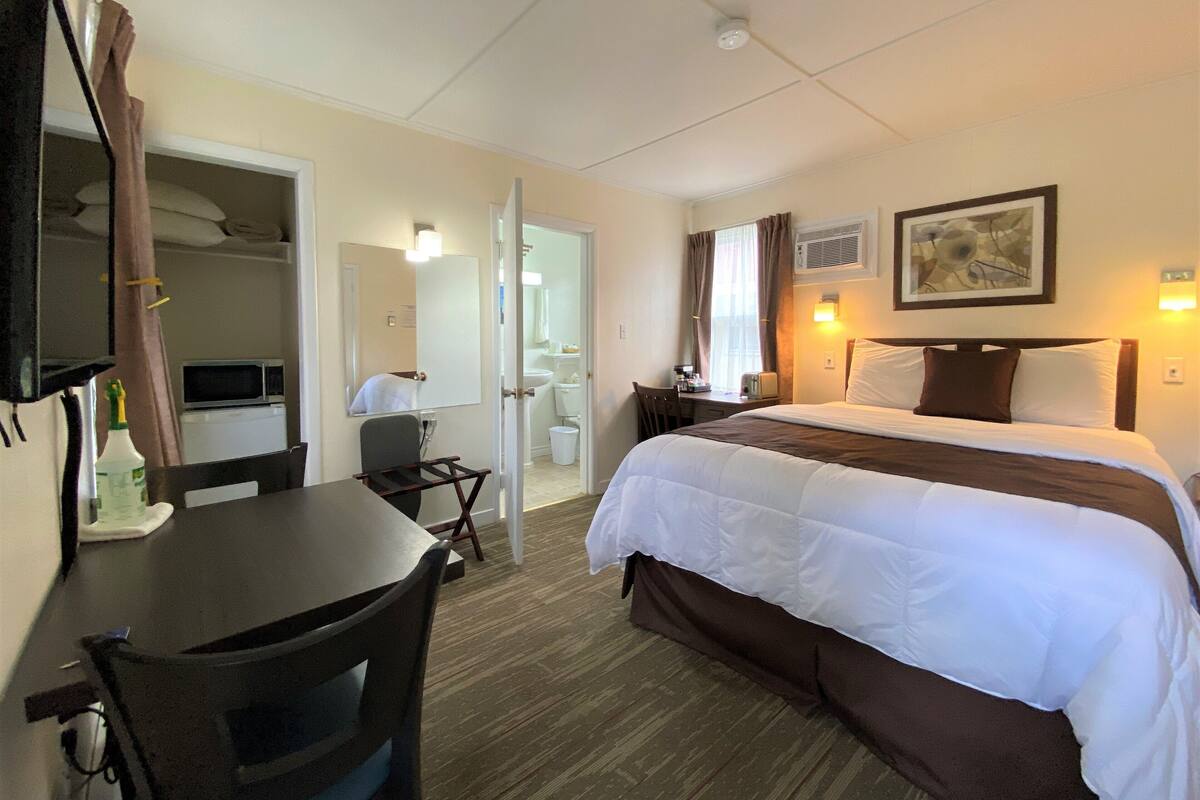 A hotel room with a bed, desk, chair, and a bathroom visible through an open door.