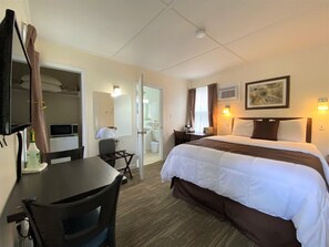 A hotel room with a bed, desk, chair, and a bathroom visible through an open door. - Coastal Inn Antigonish (Lower South River)