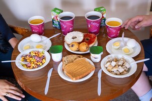 Una mesa redonda de madera con diversos alimentos para el desayuno, como cereal, huevos, tostadas y tazas de café.