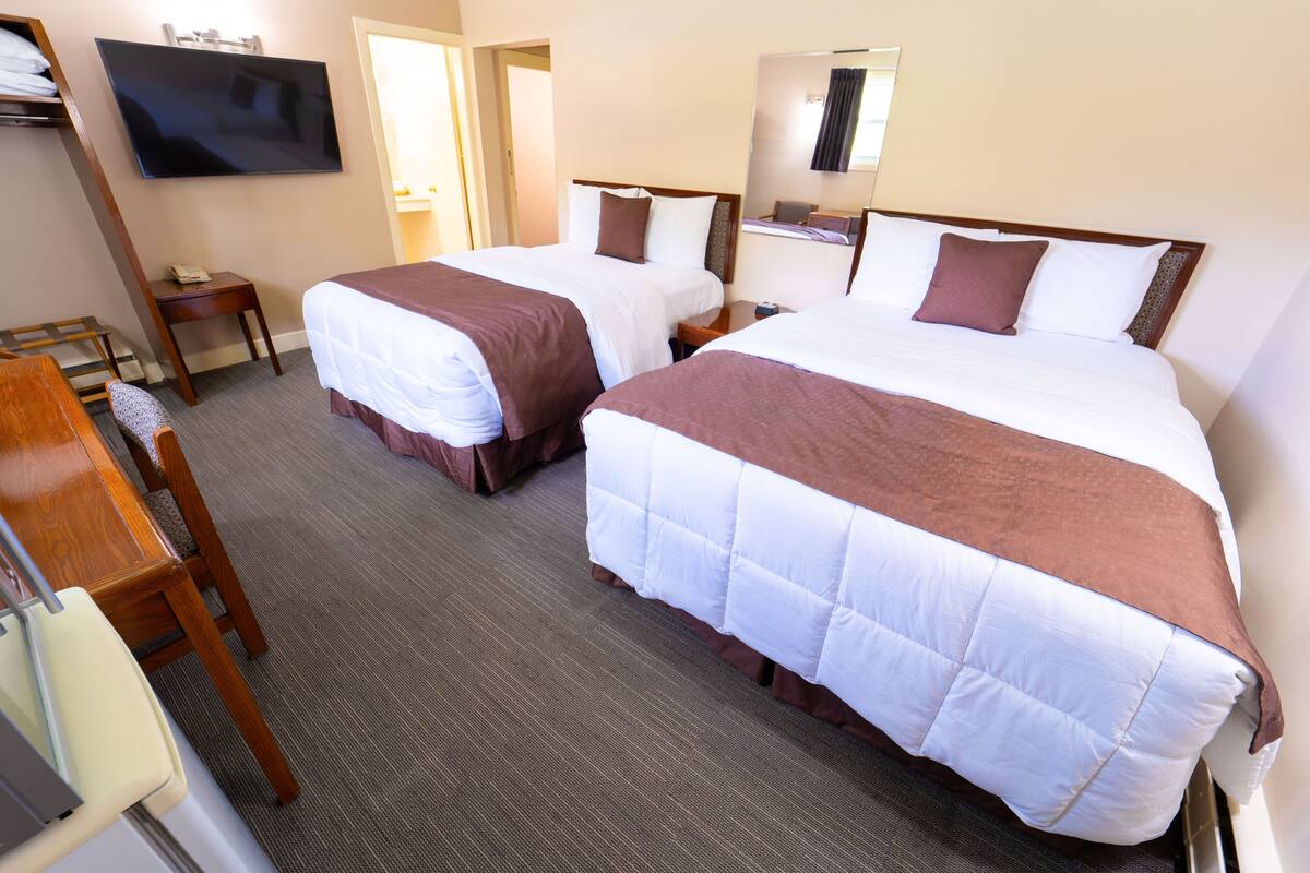 A hotel room with two beds, a TV, a desk, and a chair.