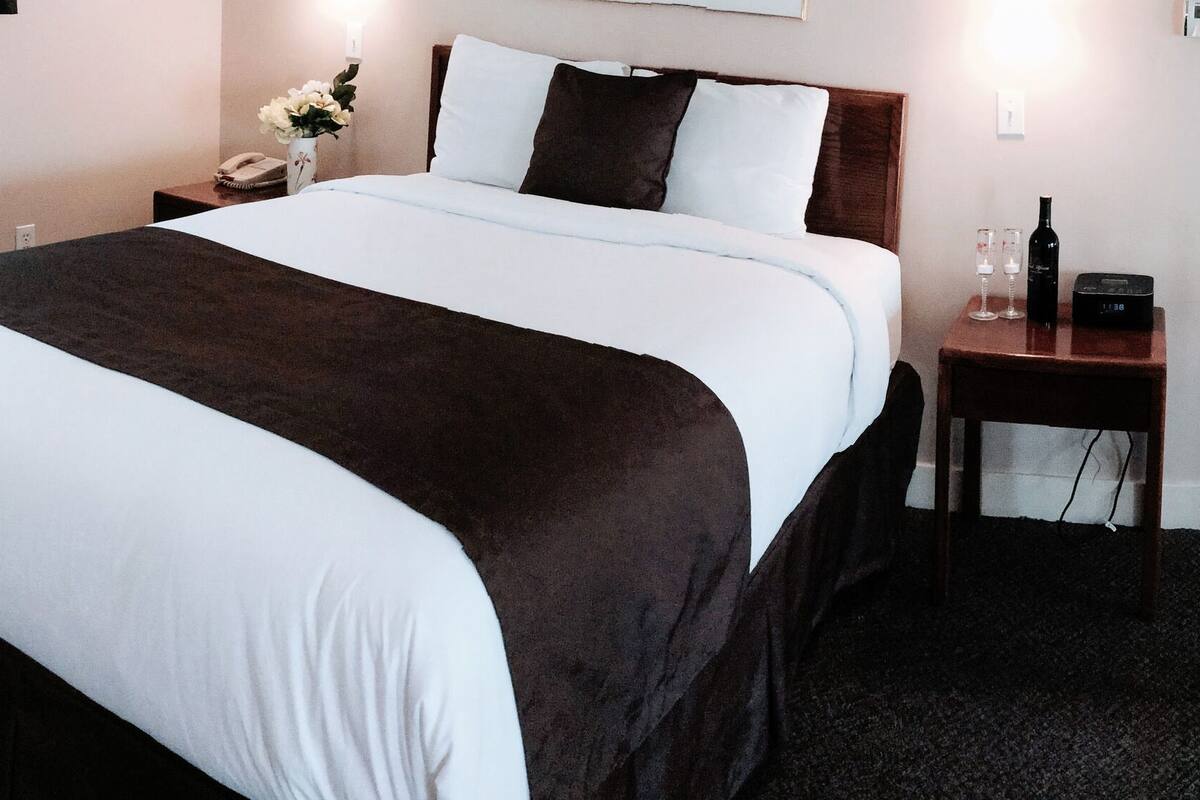 A hotel room with two beds, a nightstand with a phone and a vase of flowers, a small table with a clock, and a white railing.