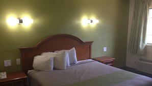 A hotel room with a wooden headboard, a bed with white pillows, two bedside tables, and wall-mounted lights. - Red Carpet Inn New Brunswick (New Brunswick)