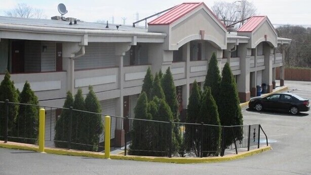 A motel with a red roof, multiple balconies, and a parking lot with a yellow safety line. - Red Carpet Inn New Brunswick (New Brunswick)