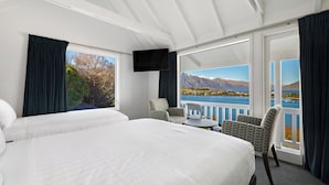 Quarto de hotel com duas camas, televisão, varanda com vista para montanhas e água, e cadeiras estampadas.