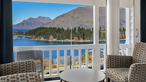 Uma varanda com vista para um lago e montanhas, mobiliada com cadeiras estampadas e uma mesa pequena.