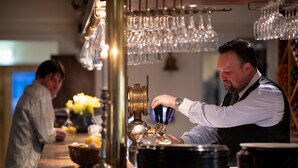 A bar setting with a bartender preparing drinks, a wine rack, and a basket of lemons. - Utö Värdshus (Uto)