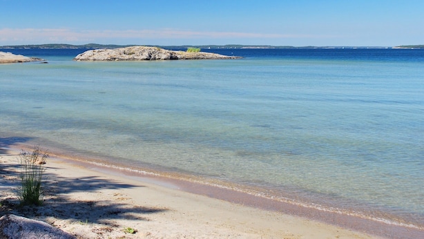 A beach with clear water, a sandy shore, and a rocky outcrop in the distance. - Utö Värdshus (Uto)