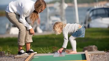 Deux personnes jouant à un jeu de société à l’extérieur, avec un port de plaisance et des bateaux en arrière-plan.