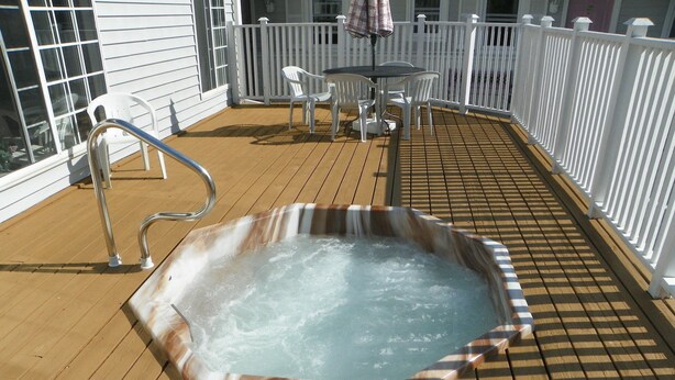 A hot tub on a wooden deck with a white railing and a table with chairs.