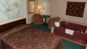 A hotel room with a large bed, a sitting area with a chair and a table, a bathtub, and floral wall decorations.